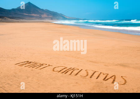 Le texte joyeux noël écrit dans le sable d'une plage Banque D'Images