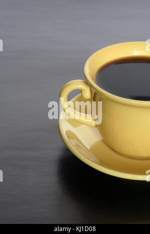 Gros plan du tasse jaune chaud avec du café noir sur fond sombre Banque D'Images