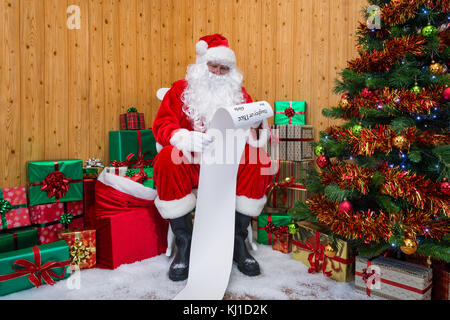 Le père Noël dans sa grotte entouré par un arbre de Noël avec des cadeaux et des boîtes de contrôle du gift wrapped Gentil ou méchant liste Banque D'Images