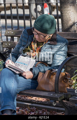 Une femme plus âgée travaille sur un journal de mots croisés en père Parc de démonstration à Greenwich Village, Manhattan, New York City Banque D'Images