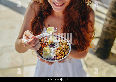 Young woman eating a l'açaï dans un bol, avec la banane, l'écrou et le tapioca. une nourriture typiquement tropical. Banque D'Images