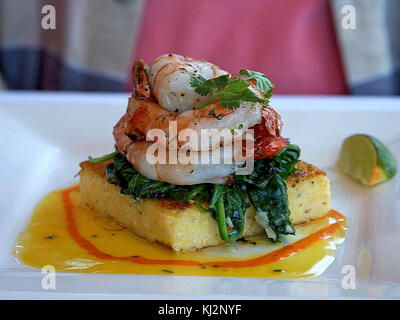 Ce plat comprend des crevettes servies avec une base de polenta et d'épinards, offrant un mélange de saveurs de fruits de mer et de légumes. Le repas met en avant des ingrédients simples et sains pour une assiette équilibrée. Banque D'Images