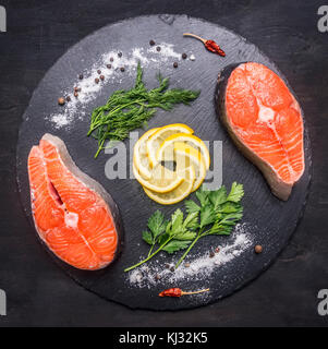 Deux matières Pavé de saumon sur une planche à découper en pierre avec sel, poivre, herbes et citron, bordée tout autour, en vue d'en haut Banque D'Images