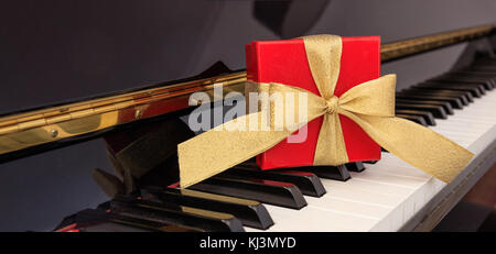 Boîte cadeau rouge avec archet d'or sur un clavier de piano classique Banque D'Images