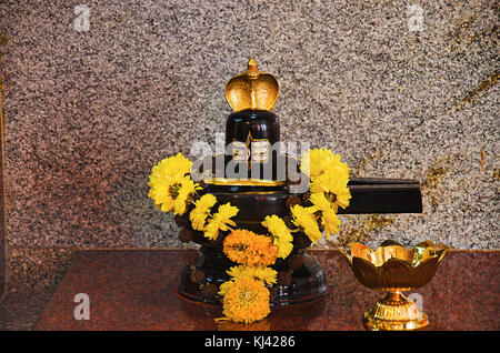 Shivling noir avec fleur jaune garland . Un traditionnel petit ou allumé Diya lampes en laiton. Patit Pavan Sri Ram Mandir, Belgavi, Karnataka, Inde Banque D'Images