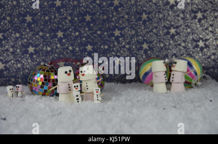 Fun noël nourriture photographie image à l'aide de guimauves en forme de bonhomme heureux avec le sourire glacé et debout dans la neige avec des boules de couleurs et d'étoiles Banque D'Images