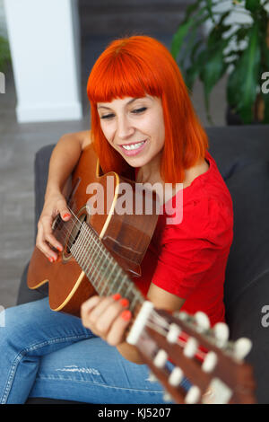 Femme redhaid détendue à jouer de la guitare dans sa maison. Banque D'Images