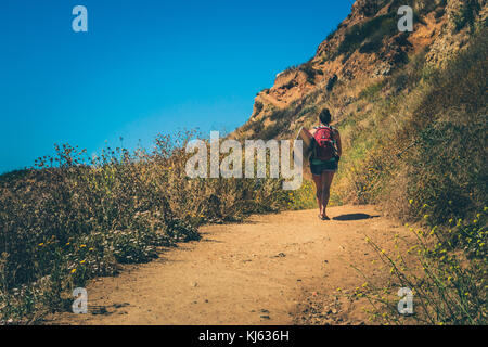 Female surfer carrying surfboard marcher le long d'un sentier de terre sur les falaises dangereuses de Palos Verdes Estates, Californie Banque D'Images