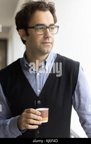 Portrait d'un homme tenant une tasse de café en papier, portant des lunettes, la pensée, vue de profil. Banque D'Images
