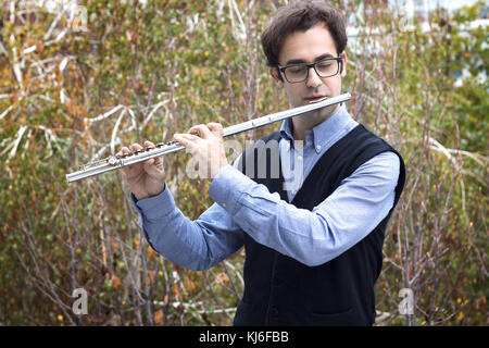 Un homme jouant un flûtiste flûte traversière en argent à l'extérieur, portant des lunettes. Banque D'Images