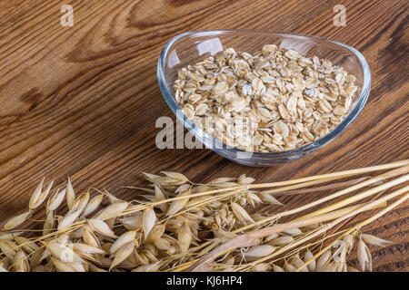L'avoine et flocons sur une table en bois. les oreilles et sec bol en verre ovale avec des flocons d'avoine sur la beauté fond brun. Banque D'Images
