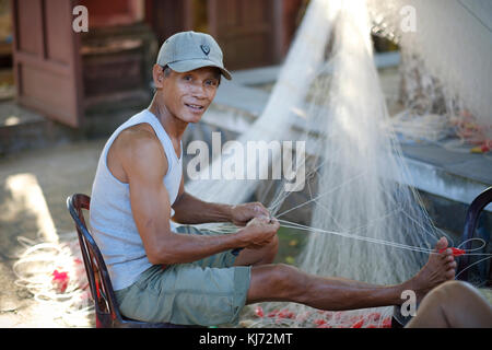 Pêcheur vietnamien la réparation de son filet de pêche dans un village côtier Banque D'Images