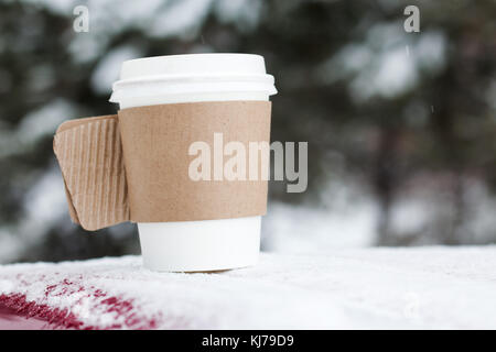 Boisson chaude dans la tasse de papier avec de la neige sur fond lumineux Banque D'Images