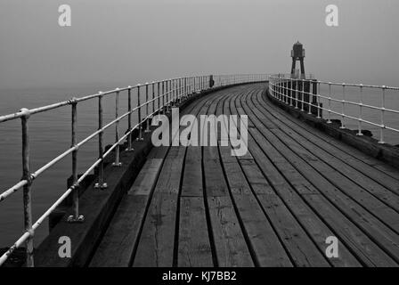 Whitby Pier dans la brume en noir et blanc Banque D'Images