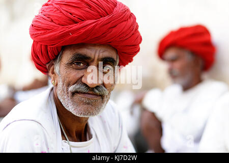 Portrait d'un homme âgé de Rabari tribu avec turban rouge et ses amis dans le dos, Rjasthan, Inde. Banque D'Images