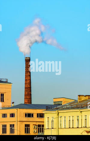 La chaufferie ville tube de brique rouge avec de la fumée blanche contre le ciel bleu clair. Banque D'Images