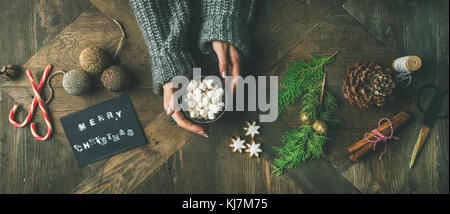 Noël, préparation du nouvel an. Plat de carte de voeux, jouet étincelant, les mains de femme en chandail gris tenant une tasse de chocolat chaud, cin Banque D'Images