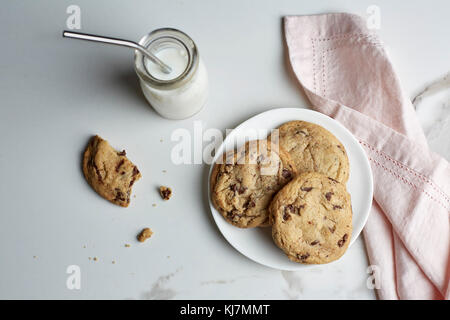 Cookies aux pépites de chocolat sur une plaque et le lait dans une bouteille en verre vintage avec une paille Banque D'Images