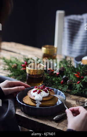 Table de petit déjeuner de Noël : femme mangeant des crêpes de citrouille avec de la crème de yaourt et du cassis Banque D'Images