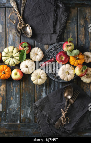 Décoration de table d'automne avec citrouilles décoratives, pommes, feuilles rouges avec coutellerie vintage, vin rouge, bougie sur table en bois. Rustique Banque D'Images