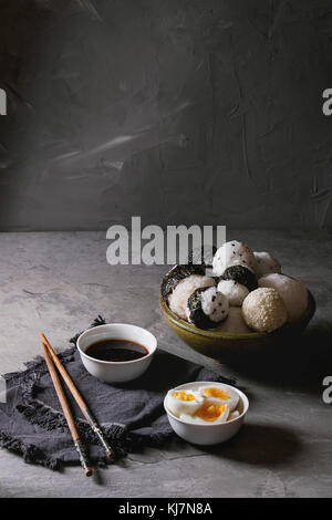 Bol avec différentes tailles de boules de riz et sésame noir avec des Algues Nori, servi avec des œufs durs, de la sauce de soja, des baguettes sur le tableau gris. Asian sty Banque D'Images
