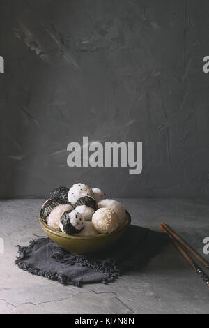 Bol avec différentes tailles de boules de riz et sésame noir avec des Algues Nori, servi avec des œufs durs, de la sauce de soja, des baguettes sur le tableau gris. Asian sty Banque D'Images