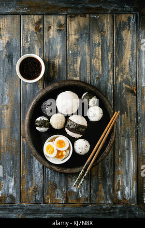 Bac en pierre de taille différente avec des boules de riz et sésame noir Algues Nori, servi avec des œufs durs, de la sauce de soja, baguettes sur planche en bois ba Banque D'Images