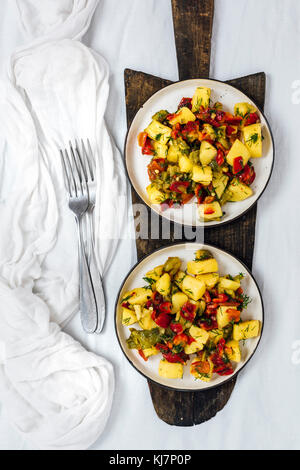 Vegan salade de pommes de terre et de poivrons grillés servis sur deux plaques photographié sur une planche à découper en bois sur fond blanc en vue de dessus. Deux chariots Banque D'Images