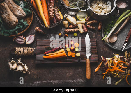 Carottes tranchées colorés à l'aide d'un couteau sur une planche à découper en bois table de cuisine rustique sur l'arrière-plan avec des légumes-racines ingrédients pour végétariens savoureux co Banque D'Images