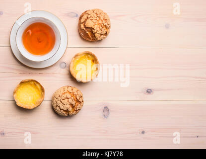 Des petits pains fraîchement cuits au four avec de la crème et le citron se trouvent autour d'une tasse de thé sur un fond en bois rustique, un espace réservé au texte Banque D'Images