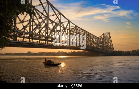 Howrah Bridge au lever du soleil avec moody sky et bateau en bois sur la rivière Hooghly. Banque D'Images