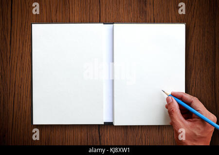 La main de l'utiliser au crayon bleu pour écrire sur l'ordinateur portable ouvert sur une table en bois brun avec l'espace blanc pour l'affichage de textes ou quelque chose Banque D'Images