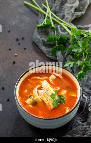 Soupe aux tomates avec des pâtes et du poulet dans un bol sur une pierre sombre arrière-plan. Le concept d'une saine alimentation. Copier l'espace. Banque D'Images