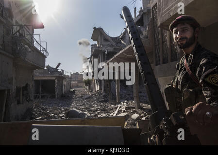 Raqqa, Syrie. 12 août 2017. Le combattant kurde des YPG se tient sur le Humvee alors que la fumée d'une frappe aérienne de la coalition fleurit derrière lui. À l’été 2017, les Forces démocratiques syriennes (FDS) ont lancé une bataille contre l’Etat islamique à Raqqa afin de reprendre le contrôle de la ville aux mains de l’organisation terroriste. L'opération a fait au moins 3000 morts, y compris des combattants des deux côtés et des civils. Crédit : Jake Simkin/SOPA/ZUMA Wire/Alamy Live News Banque D'Images