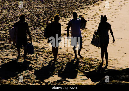 Silhouette de quatre amis marchant sur la plage au coucher du soleil. deux couples projettent de grandes ombres sur le sable comme ils head home après journée sur la plage. Banque D'Images