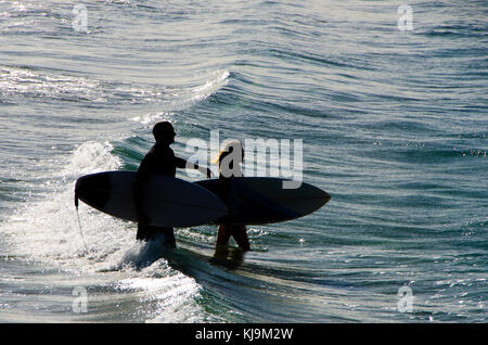 La figure de l'homme solitaire walking on beach with surfboard. Silhouette d'homme casting surfeur de longues ombres sur le sable pendant qu'il marche dans votre plage au coucher du soleil. Banque D'Images