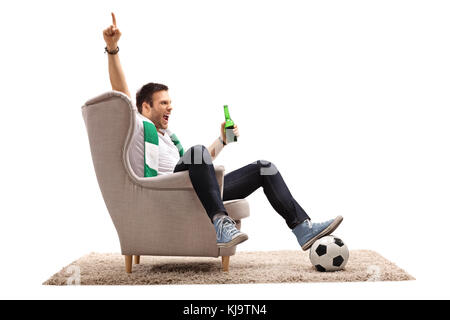 Heureux fan de football avec un foulard et une bouteille de bière assis dans un fauteuil vers le haut avec son doigt isolé sur fond blanc Banque D'Images