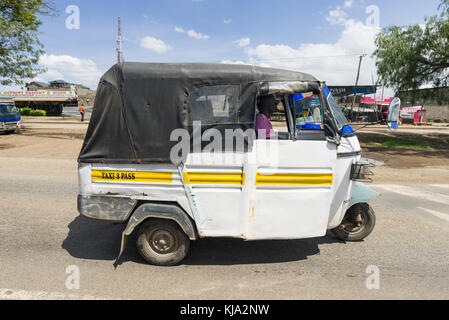 Un trois-roues blanc tuk tuk taxi roulant sur la route à travers une petite ville, Kenya, Afrique de l'Est Banque D'Images