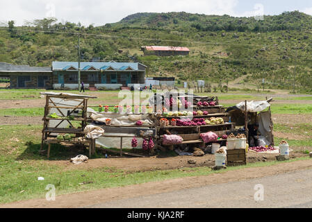 Une femme africaine est assis par son étal de fruits et légumes en vente sur le bord de la route, Kenya, Afrique de l'Est Banque D'Images