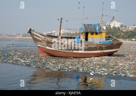 Bateau de pêche en bois sur la plage parmi les déchets en plastique à Mumbai, Inde Banque D'Images