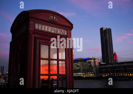 Téléphone traditionnel anglais boîte rouge à Londres avec coucher du soleil reflétée dans windows. Banque D'Images