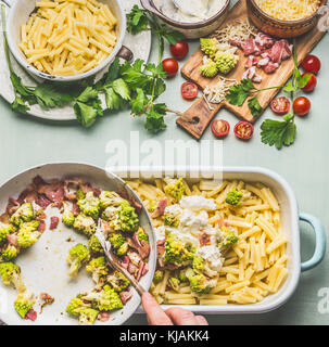 Femme femmes la cuisson des pâtes cocotte au jambon et chou romanesco rôties en sauce crémeuse sur table de cuisine avec des ingrédients de base, haut Banque D'Images