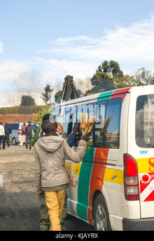 African Male camelots essaient de vendre le maïs cuit à passagers dans un minibus par la route de matatu, Kenya, Afrique de l'Est Banque D'Images