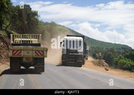 Les camions roulant sur une route poussiéreuse à travers l'escarpement de la vallée du Rift avec les gens se tenant au bord de la route, Kenya, Afrique de l'Est Banque D'Images