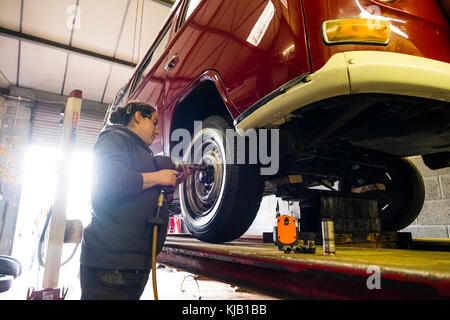 Une femme mécanicienne travaillant dans un petit atelier de garage indépendant, remplaçant les roues d'un campervan Volkswagen VW 1970 classique de type 2, Royaume-Uni Banque D'Images