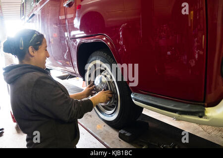 Une femme mécanicienne travaillant dans un petit atelier de garage indépendant, remplaçant les roues et les enjoliveurs d'un campervan Volkswagen VW 1970 classique de type 2, Royaume-Uni Banque D'Images