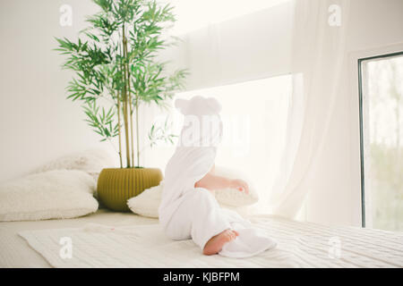 beau bébé garçon souriant recouvert d'une serviette en bambou blanche avec des oreilles amusantes. Assise sur un intérieur en laine à carreaux blanc. Banque D'Images