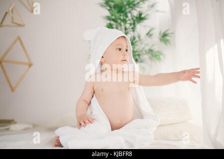 beau bébé garçon souriant recouvert d'une serviette blanche avec des oreilles amusantes. Assise sur un intérieur en laine à carreaux blanc. Banque D'Images