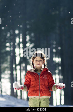 Jeune fille debout frontale et tenant des boules de neige dans ses mains, souriant joyeusement. Heure d'hiver Banque D'Images