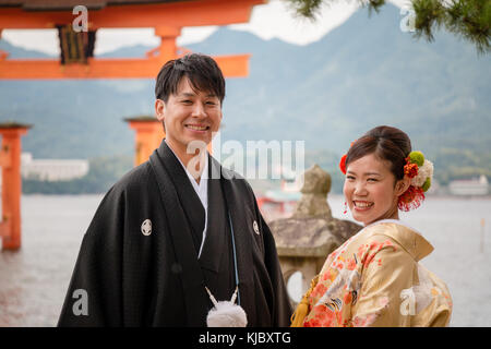 Newlywed couple japonais en face de la porte torii flottant, Miajima, Japon Banque D'Images